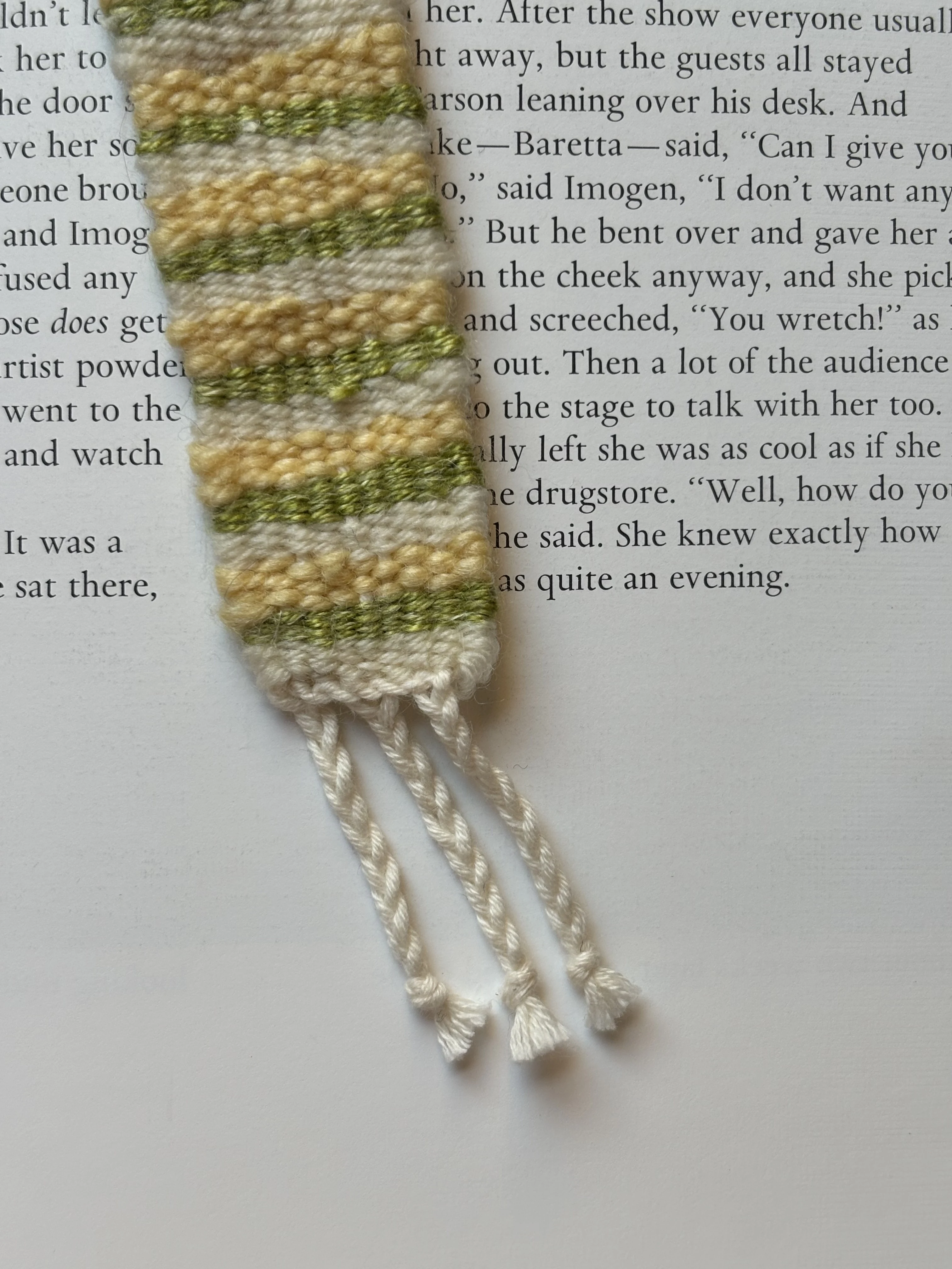 Close-up of a cream, yellow, and green woven bookmark on an open book